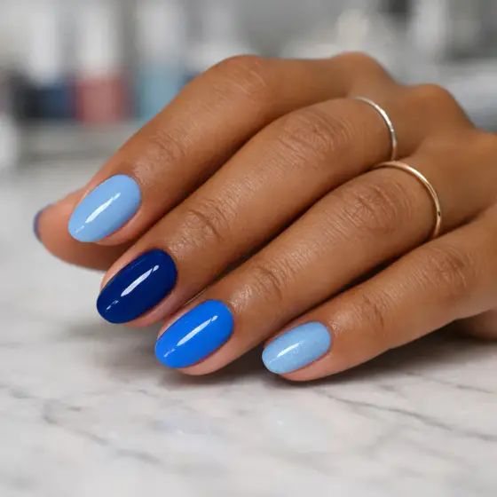 Uñas cortas redondeadas pintadas en varios tonos de azul brillante
